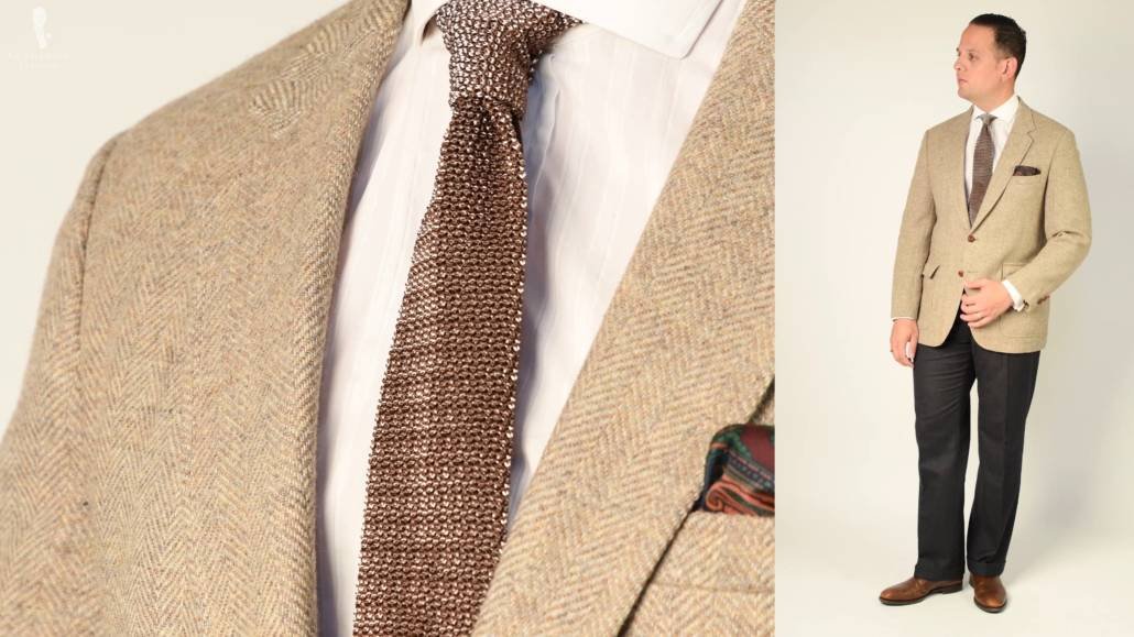 Raphael portant un pantalon de flanelle gris, un manteau de sport en tweed marron, des chaussures de ville marron et des accessoires aux nuances de marron.