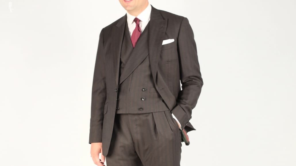 Costume trois pièces marron aux motifs subtils, chemise à col blanc, pochette de costume blanche et cravate rouge à pois pour une tenue de bureau plus formelle.