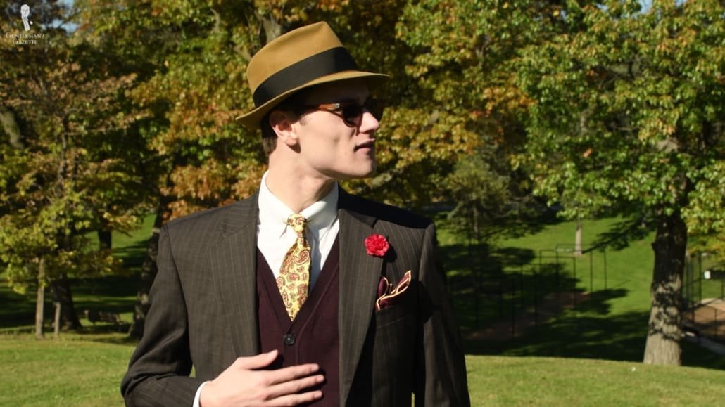Preston porte un costume à motifs marron et un cardigan bordeaux contrastant.