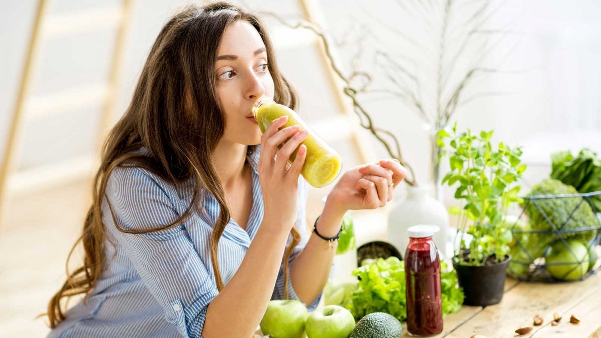 Femme buvant un smoothie avec des légumes mélangés.