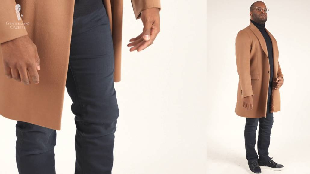 Kyle porte les baskets Lanvin avec un jean foncé, un pull à col roulé foncé et un pardessus camel.