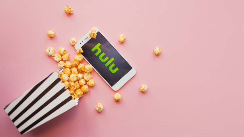 Application Hulu ouverte sur smartphone à côté d'une boîte de pop-corn éparpillée sur le sol