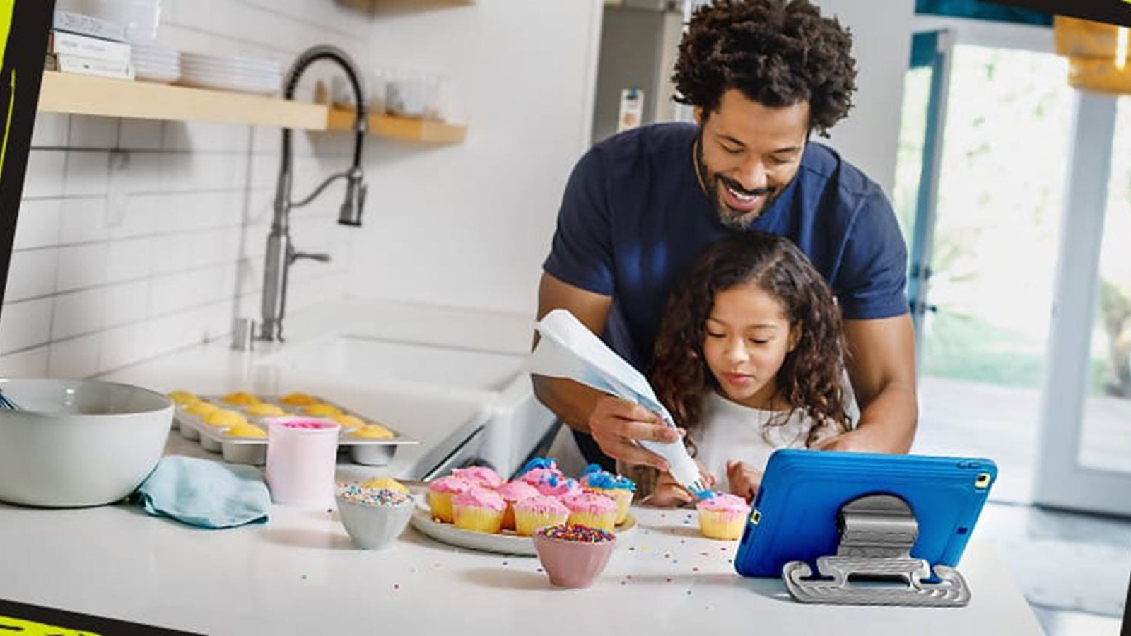 Un père et sa fille décorant des cupcakes devant un iPad dans un étui adapté aux enfants.