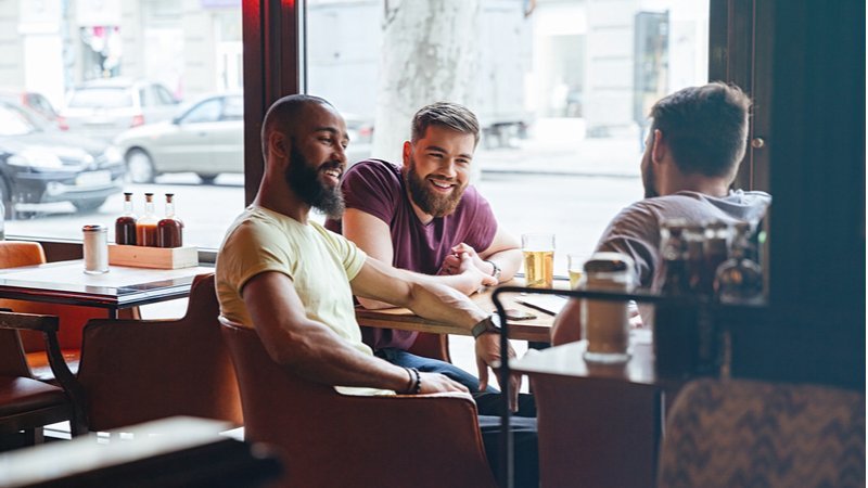 3 hommes assis à une table de café à l'intérieur en riant