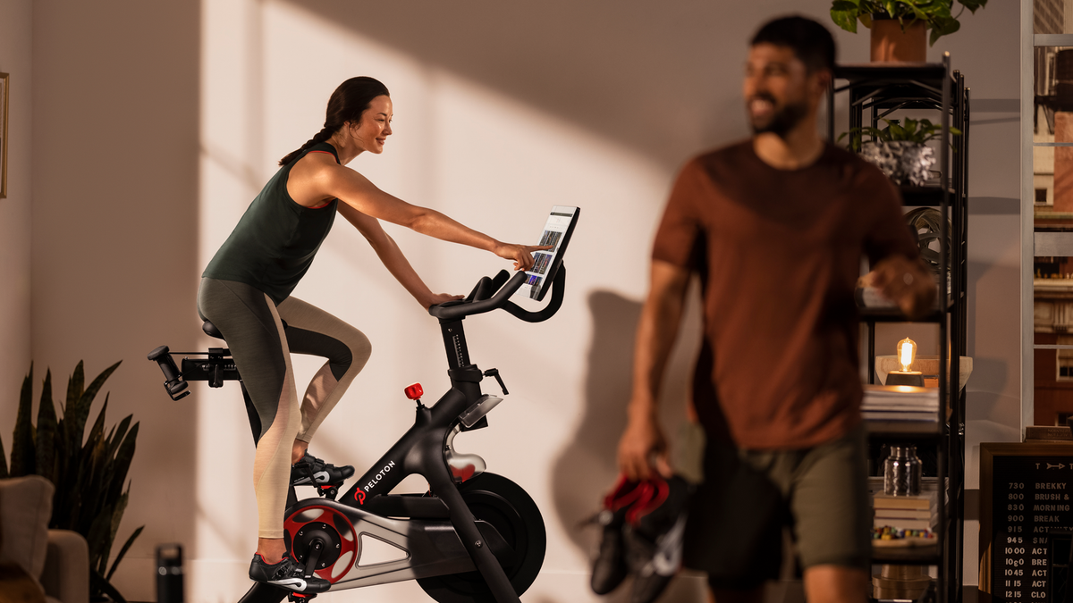 Une femme fait du vélo Peloton dans son salon.