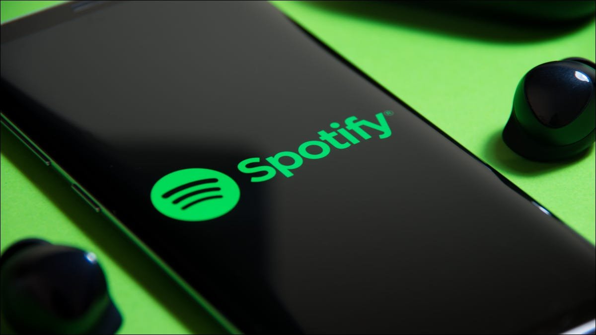 Smartphone affichant le logo Spotify à côté d'écouteurs sans fil sur fond vert.