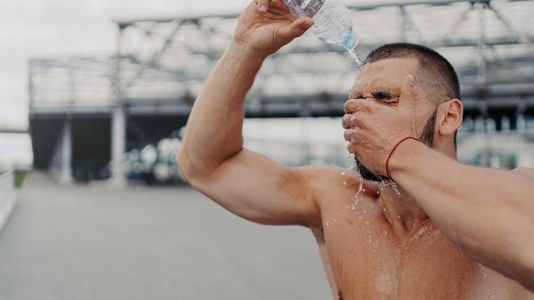 Un homme versant de l'eau sur sa tête à partir d'une bouteille d'eau