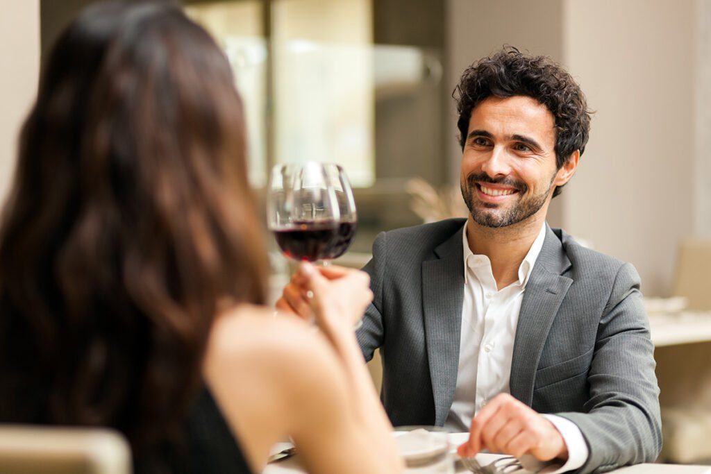 homme en costume gris souriant et portant un toast femme avec du vin