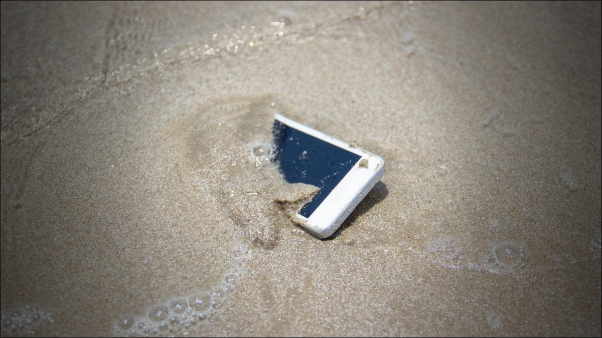 Un smartphone dans le sable de l'océan avec de l'eau salée.