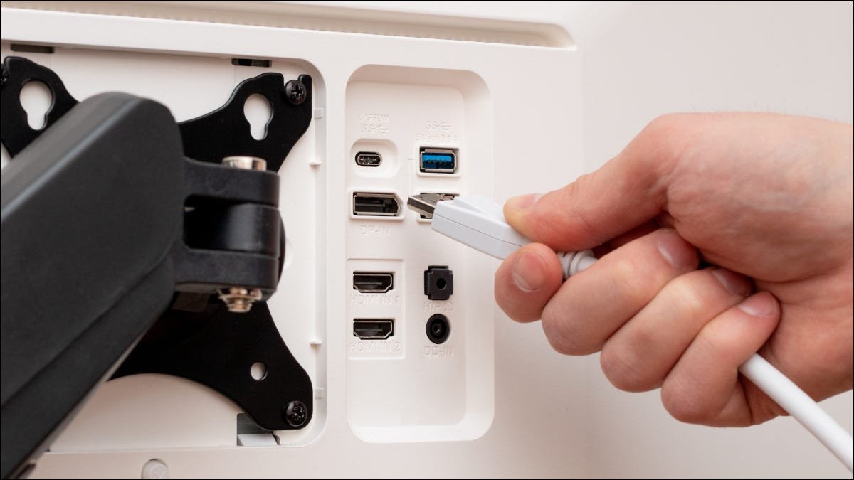 La main d'une personne branchant un câble DisplayPort à l'arrière d'un écran d'ordinateur.