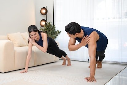 Un homme et une femme font des échanges de bras sur une planche haute à la maison, en tapotant une épaule à partir d'une position de planche haute...