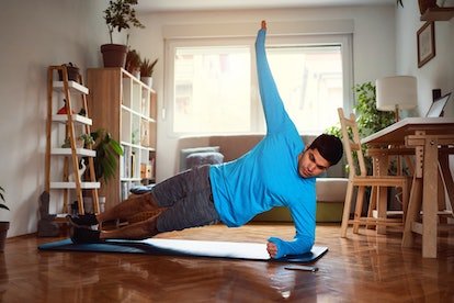 Un homme fait une planche latérale à la maison sur un tapis de yoga.