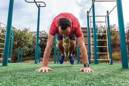 Un homme faisant des burpees à l'extérieur sur une aire de jeux.