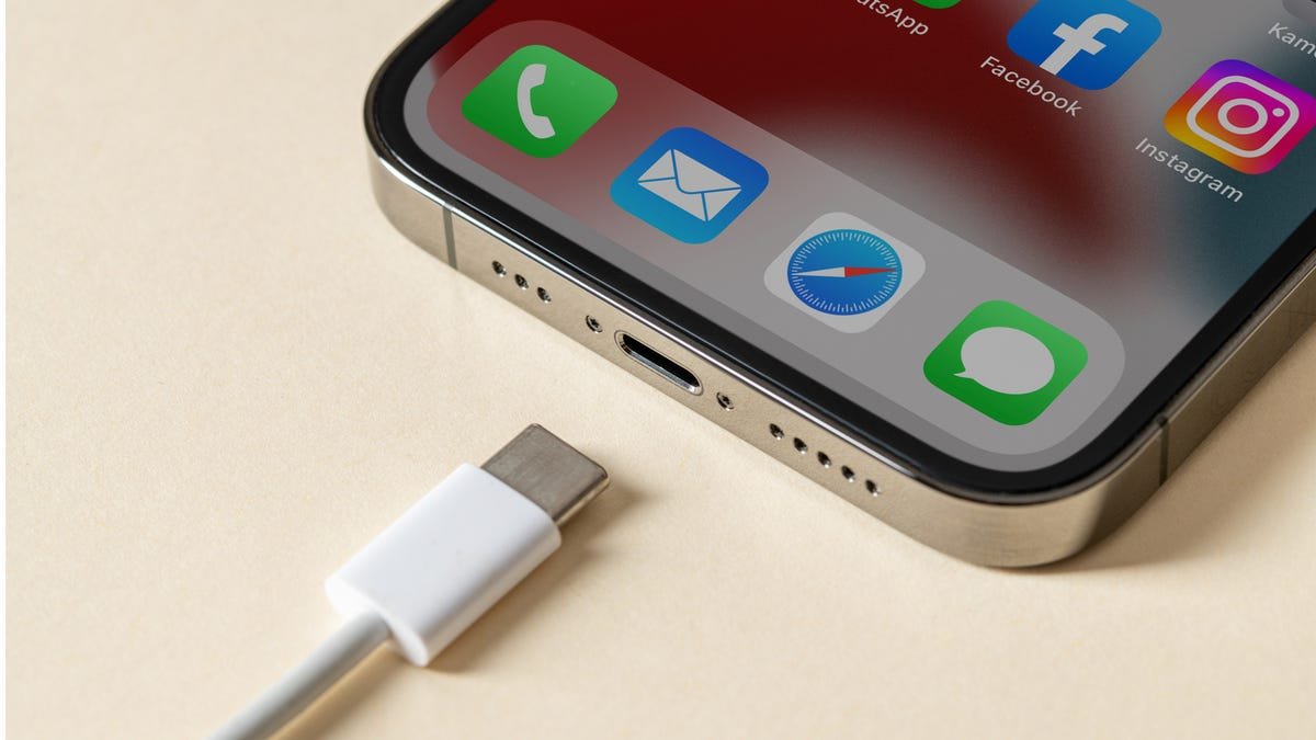 Un iPhone posé sur une table avec un câble de charge USB-C aligné avec le port de charge.