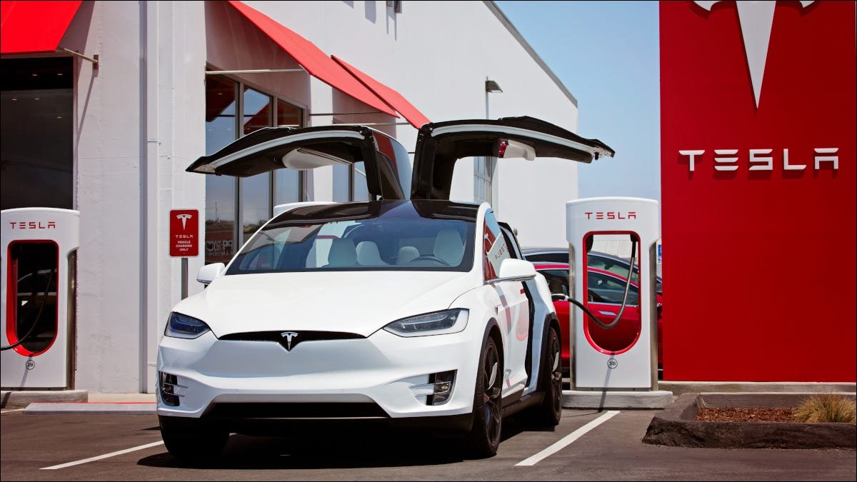 Voiture Tesla branchée sur une station de charge et avec les portes Falcon ouvertes.