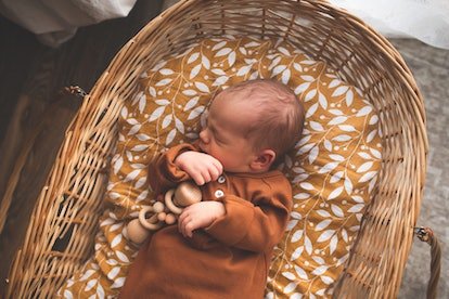 Bébé nouveau-né en salopette à la mode en coton dort dans un panier naturel en osier.