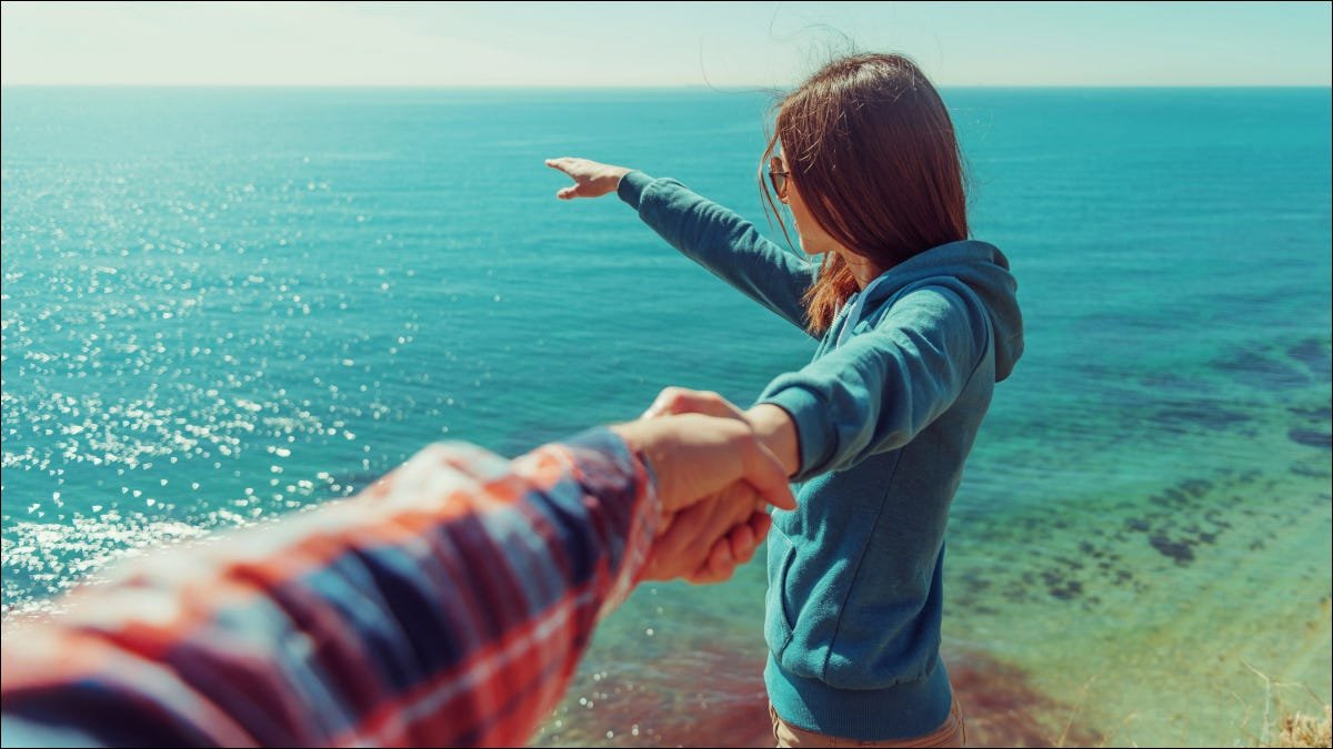 Point de vue d'une femme pointant vers l'océan tout en tenant la main d'une personne hors caméra.