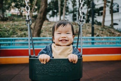 Happy baby girl smiling jouant joyeusement sur la balançoire dans l'aire de jeux