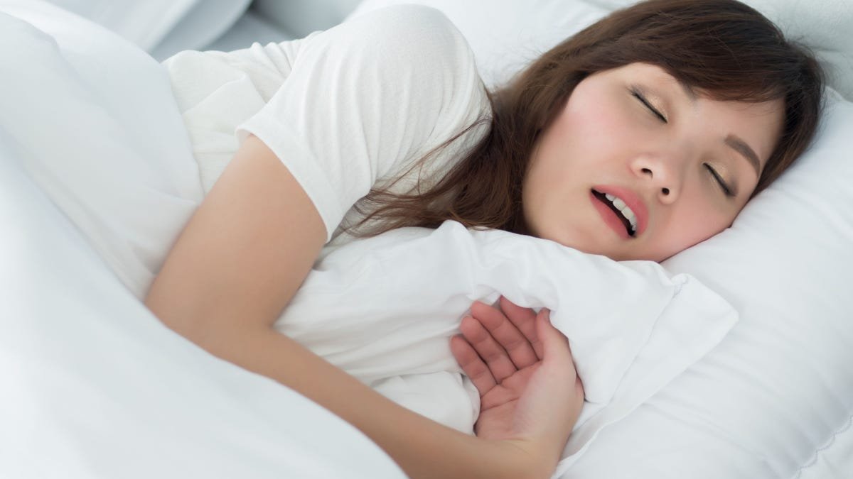 Une femme dort dans son lit la bouche ouverte.