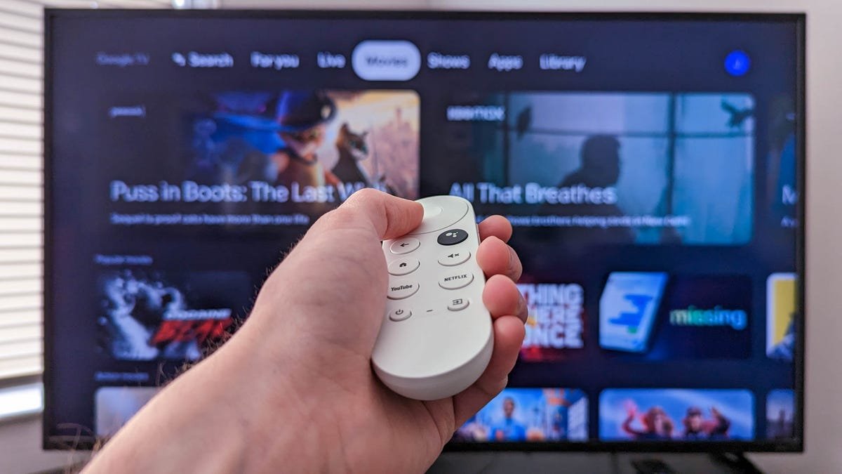 Personne tenant une télécommande Chromecast devant un téléviseur avec Google TV ouvert