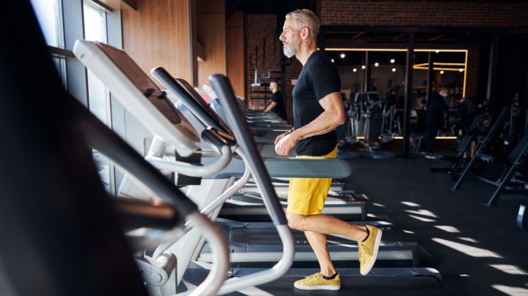 personne aux cheveux gris utilisant un tapis roulant dans une salle de sport