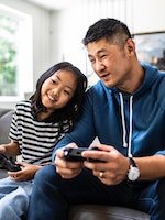 Un père et sa fille jouent ensemble à des jeux vidéo sur le canapé.