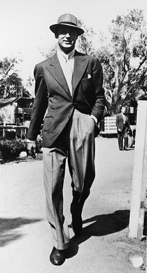 L'acteur britannique Cary Grant (1904 - 1986) marchant dehors portant une veste à fines rayures et un chapeau, années 1940.