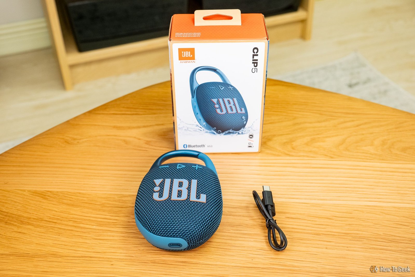 Le JBL Clip 5 avec son emballage et son câble de chargement.