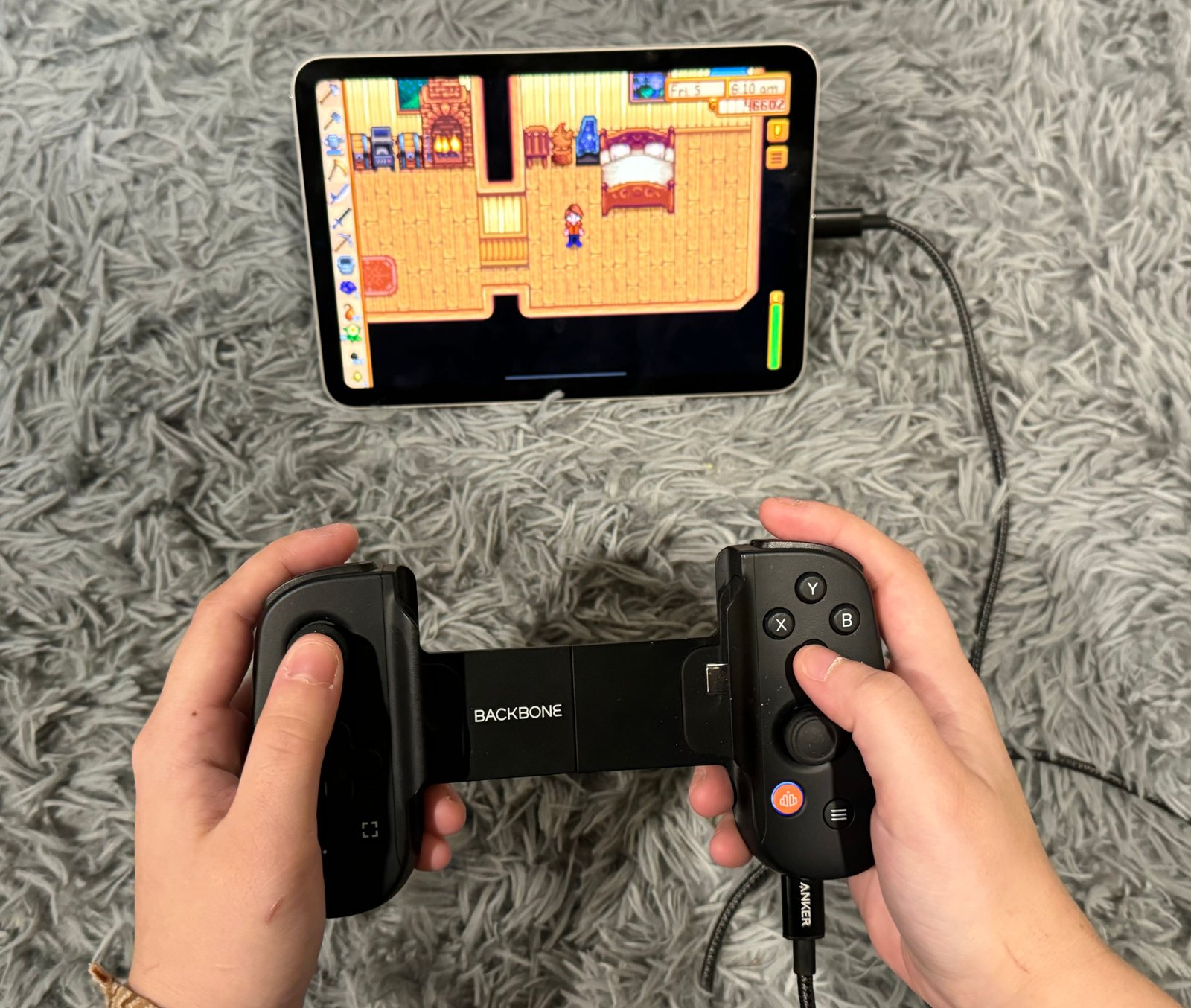 Personne tenant une manette de jeu Backbone connectée à un iPad mini, avec Stardew Valley en cours de lecture à l'écran.