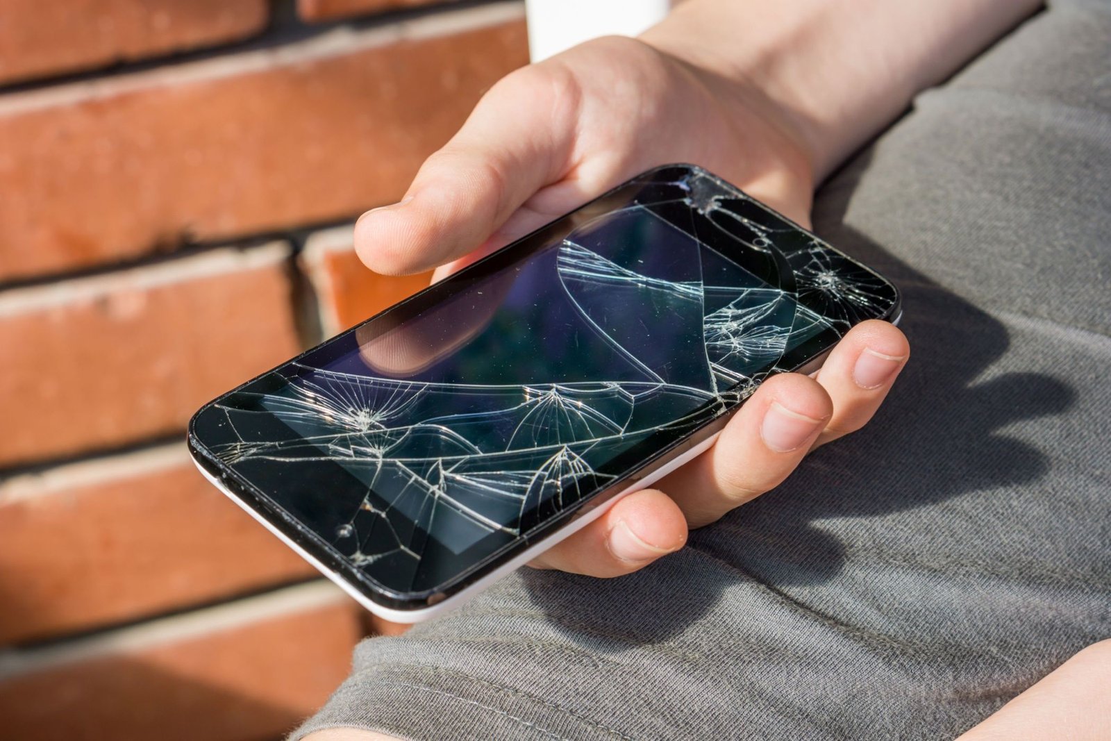 Gros plan de la main d'un garçon regardant son téléphone toujours en activité avec un écran cassé.