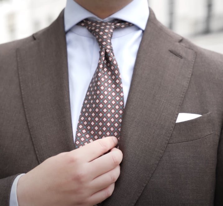 Jonas présentant sa cravate Mulani, un accessoire de fabrication italienne, caché soigneusement dans son pantalon brun sur mesure