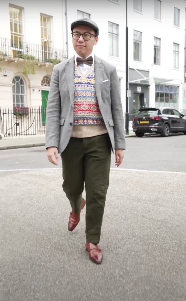 Mike Lein d'Amsterdam marchant à Londres dans un ensemble d'inspiration vintage avec un blazer gris, un pull d'île juste, un pantalon d'olive et un nœud papillon