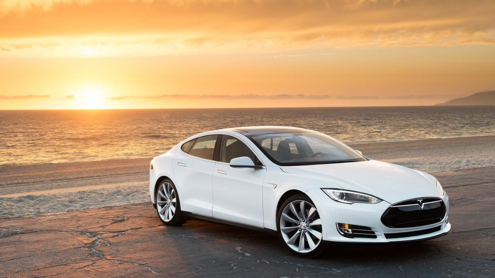 Vue avant au trois quarts d'une Tesla Model 2015 White Gared sur une plage au coucher du soleil.