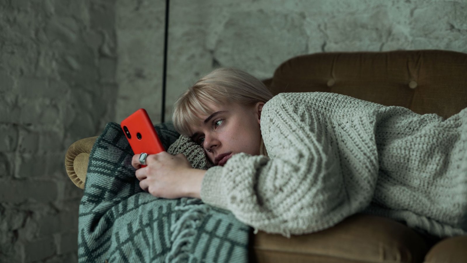 Femme allongée sur un canapé fixant un smartphone.