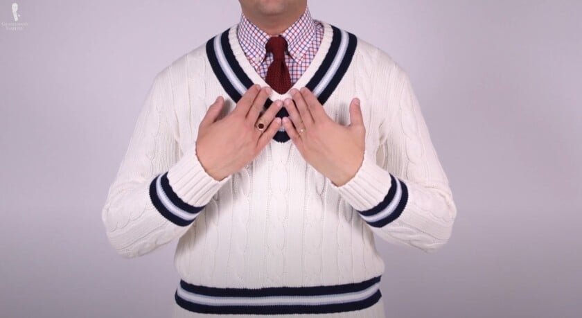 Raphael portant un pull de cricket tox-tricot blanc superposé sur une chemise de chèque et une cravate en tricot rouge