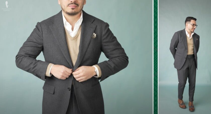 Ivan portant un costume de flanelle au charbon de bois superposé sur un pull à col en V Camel et une chemise OCBD blanche, associée à des bottes ailées beige.