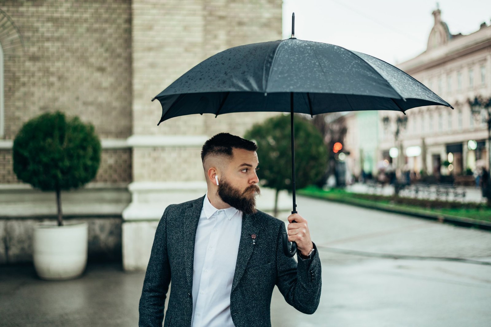 Homme portant des aérpodes sous la pluie sous un parapluie.