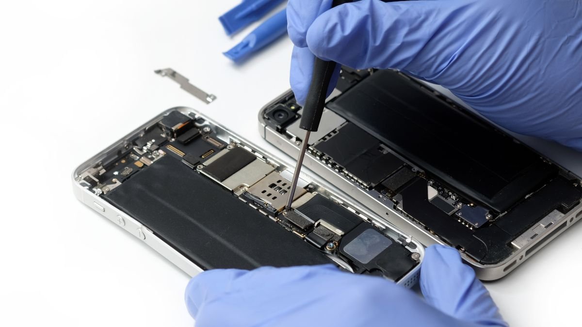Gros plan des mains gantées du technicien réparant les pièces internes d'un iPhone.