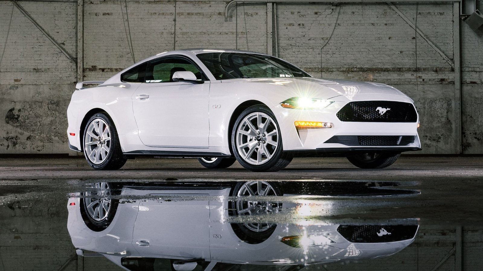 Front statique 3/4 tir d'un coupé Ford Mustang White 2022 garé dans un entrepôt avec de l'eau au sol.