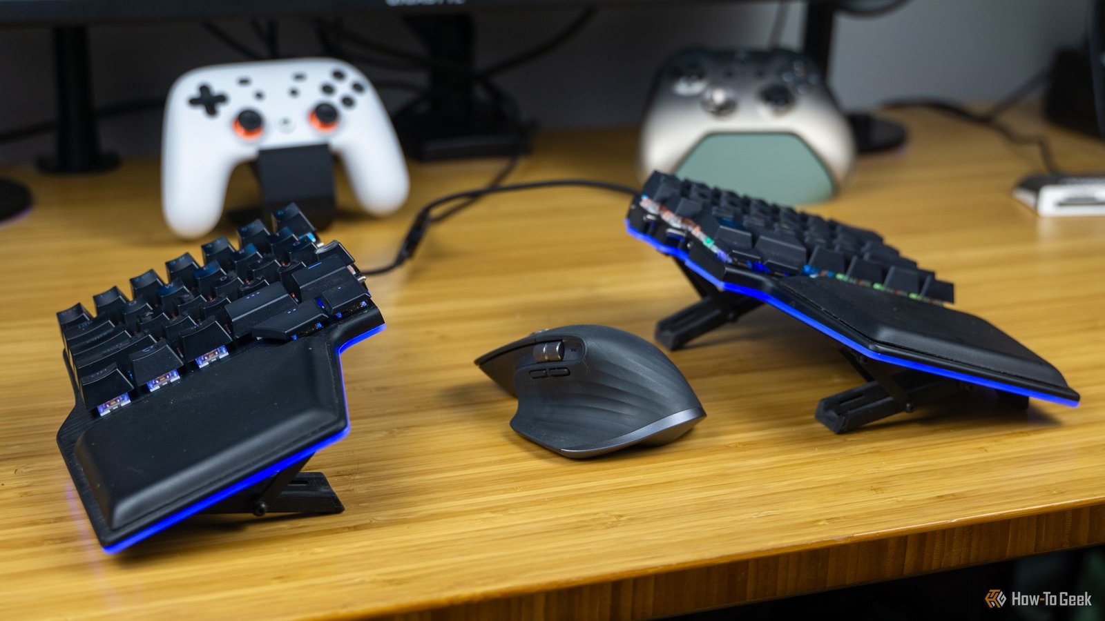 Le Dygma soulève un clavier divisé sur un bureau en bambou avec un MX Master 3 entre les moitiés et certains contrôleurs de jeu en arrière-plan.