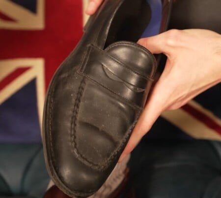 Une personne tient un mocassin de sou noir usé avec des détails visibles et de couture visibles