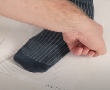 Un pied d'un homme dans des chaussettes à fines rayures de la Marine mesurées par rapport à une feuille de dimensionnement