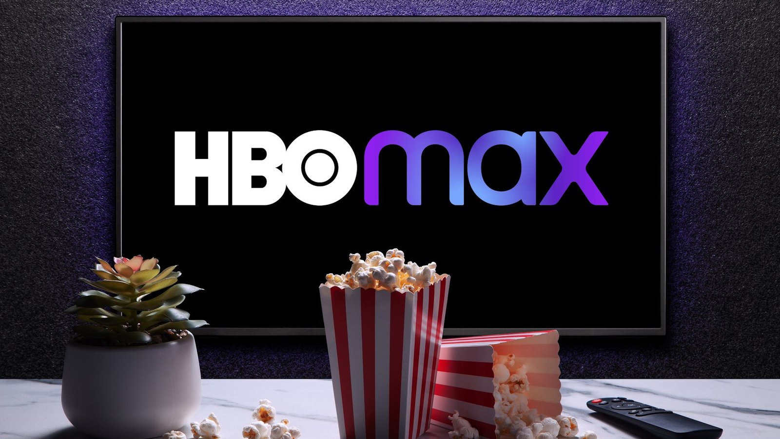 Logo HBO Max à la télévision avec des boîtes à pop-corn, une télécommande et une usine de maison sur la table.