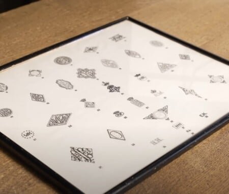 Fiche d'affichage encadrée montrant des dizaines de conceptions historiques de monogramme et de crête Kniže, posées à plat sur un comptoir en bois.