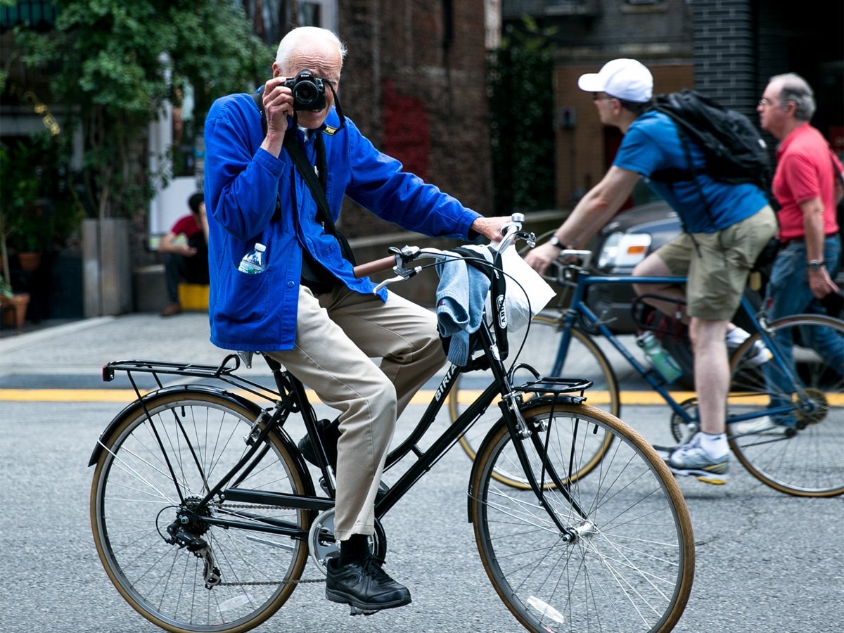 vieil homme faisant du vélo tout en prenant des photos à l'aide d'un appareil photo