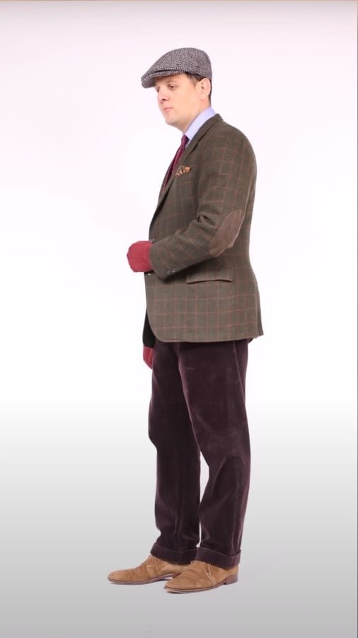 Raphael portant une casquette plate à tweed à l'olive, un manteau de sport à chevrons léger, des bouchards en bois de bordeaux et des chaussures en daim.