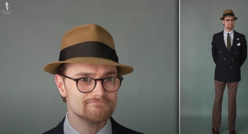 Preston portant un fedora brun moutarde et avare avec un blazer à double poitrine bleu marine, un pantalon brun et des accessoires de coordination.