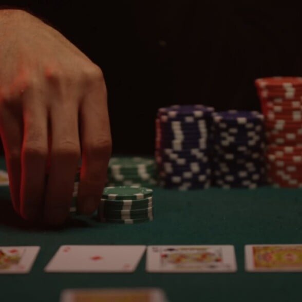 Gentleman vice Gambling pari pour le plaisir Une main plaçant des puces de poker vertes sur une table de cartes, avec des piles de puces bleues, rouges et blanches en arrière-plan et à jouer aux cartes disposées