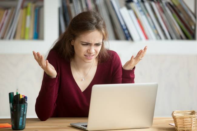 Femme qui regarde un ordinateur portable avec une expression frustrée et une main dans les airs