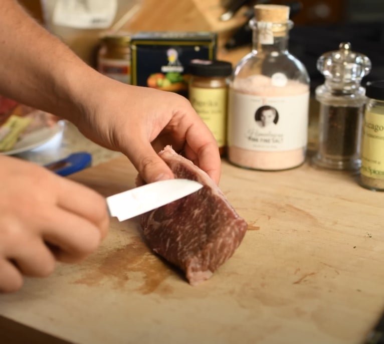 Trancher la gastronomie de bœuf wagyu Personne tranchant le bœuf wagyu marbré sur une planche à découper en bois avec des épices en arrière-plan.